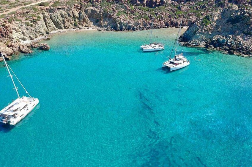 A turquoise sea with three sailboats anchored near rocky cliffs. 3