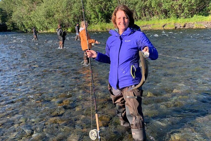 A person standing in a river holding a fish, wearing a blue jacket and brown pants. 5