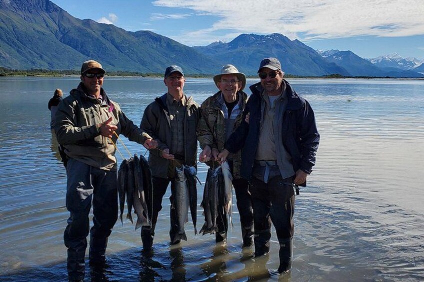 Four people standing in a lake holding fish. 1