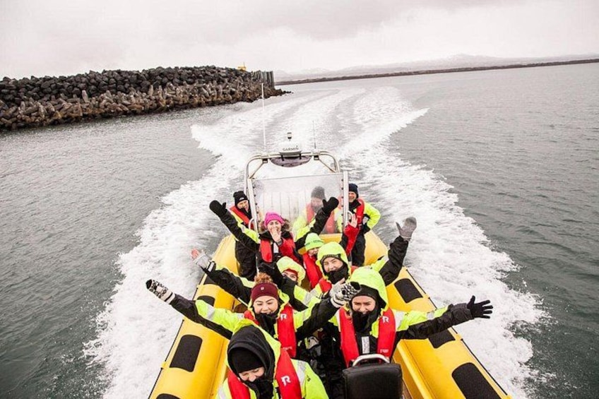 A group of people in a yellow inflatable raft on a body of water, with a rocky breakwater in the background. 1