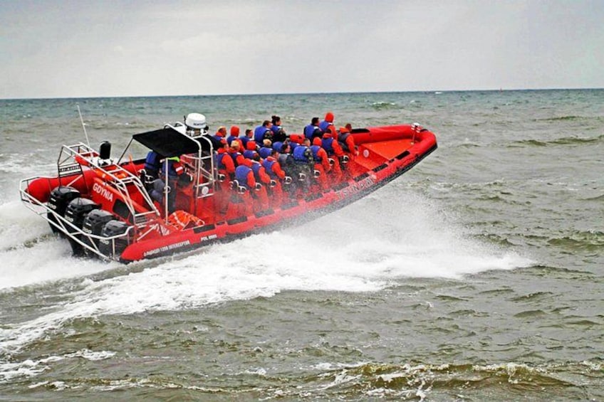 A red inflatable boat with passengers in blue life jackets on the water. 4