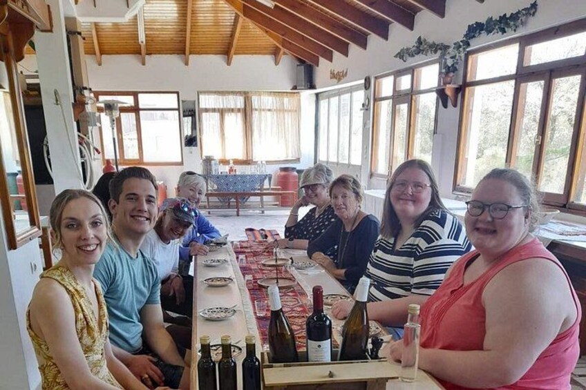 En gruppe mennesker sidder omkring et bord med flasker og glas i et rum med træbjælker og store vinduer. 2