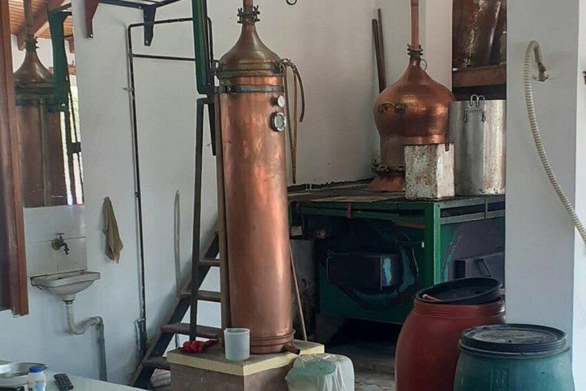 A copper distillation apparatus in a workshop with a sink, ladder, and barrels. 3
