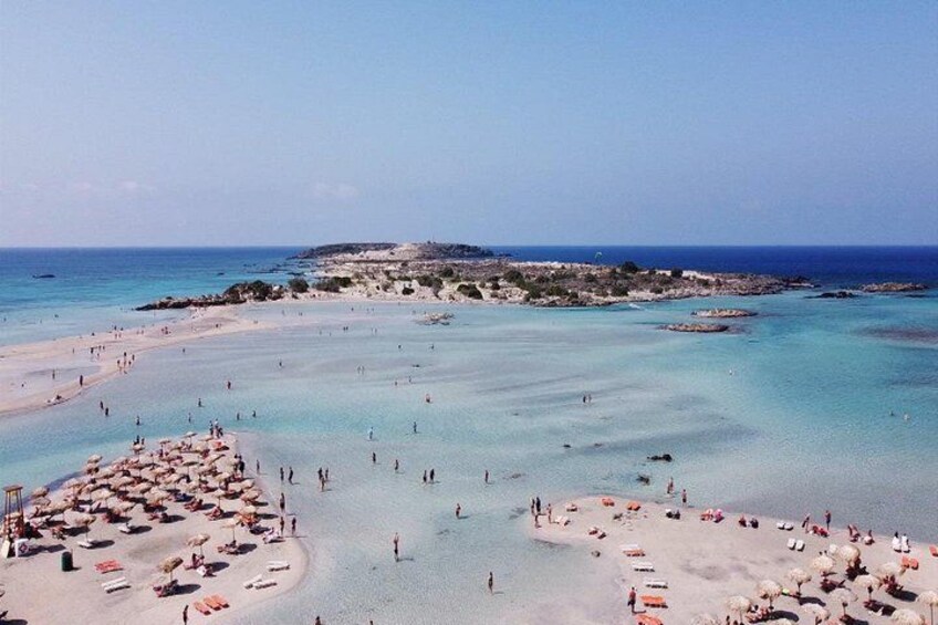 A beach with clear turquoise water, sandy shores, and a rocky outcrop in the distance. 5
