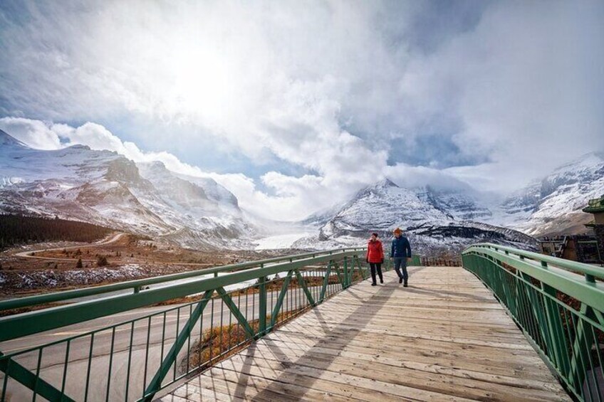 Un pont en bois avec des garde-corps verts, qui mène à un paysage montagneux enneigé. 3