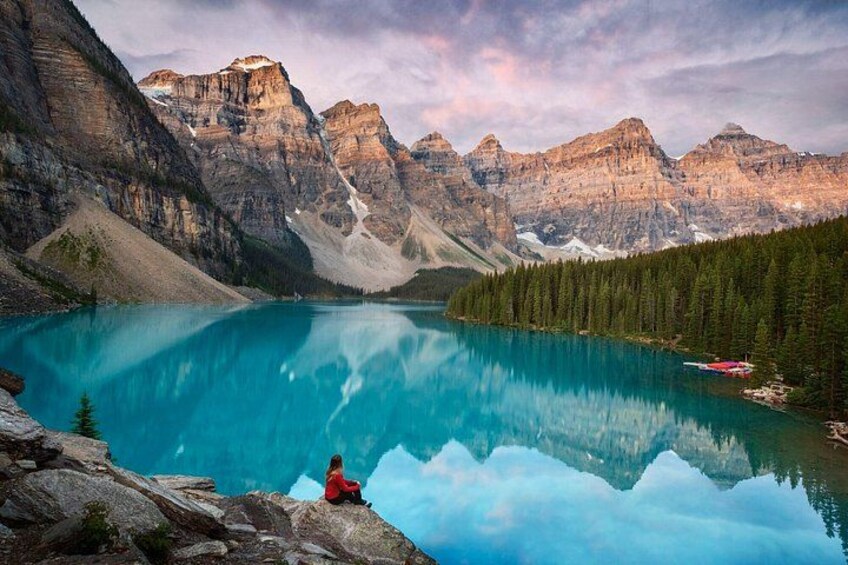 A person sitting on a rock by a turquoise lake with mountains in the background. 1