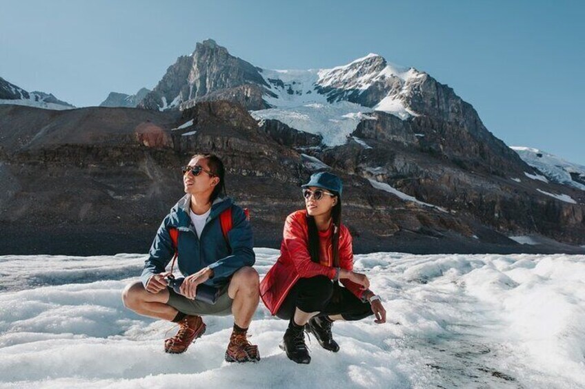 Deux personnes sont assises sur une surface enneigée, avec un paysage montagneux en arrière-plan. 2