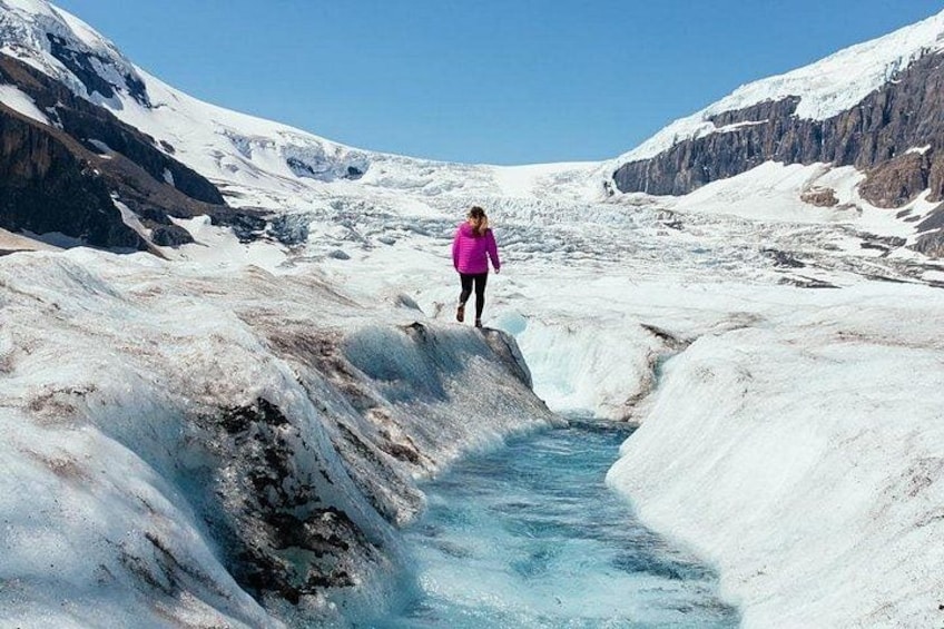 A person standing on a glacier with a river flowing through it. 3