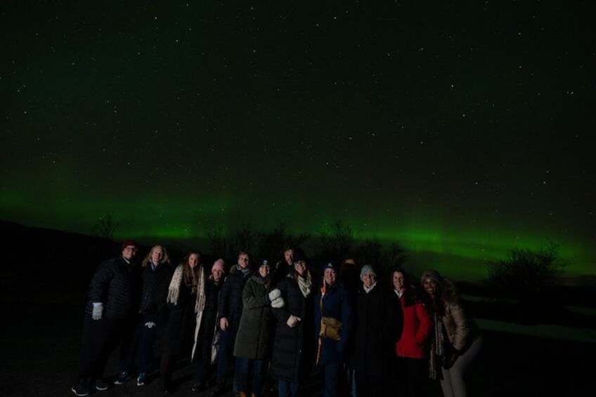A group of people standing under a night sky with visible stars and a green aurora. 5
