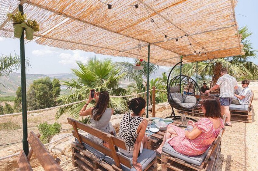 A group of people relaxing under a thatched umbrella, with a scenic view of a mountainous landscape in the background. 1