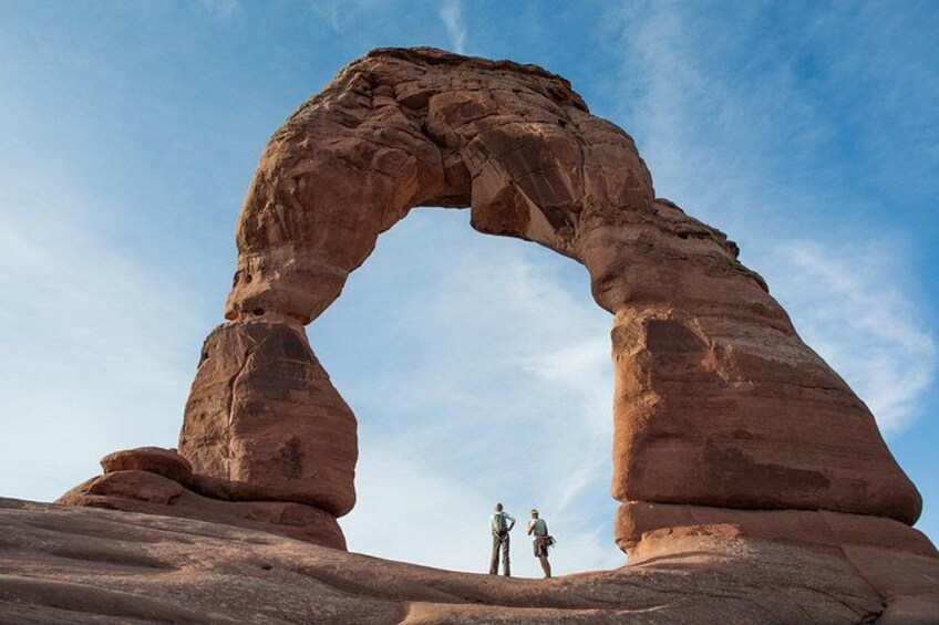A large rock arch formation with two people standing at its base. 1