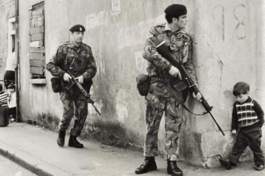 Ein Soldat in Tarnuniform hält ein Gewehr und steht neben einem Kind mit Streifenhemd, das vorbeigeht. 2