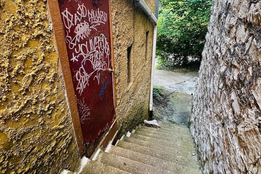 A narrow stone staircase leading to a door with graffiti. 3