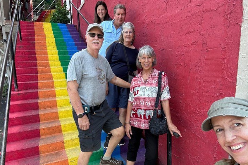 A group of people standing in front of a red wall with a rainbow-colored stairway. 5