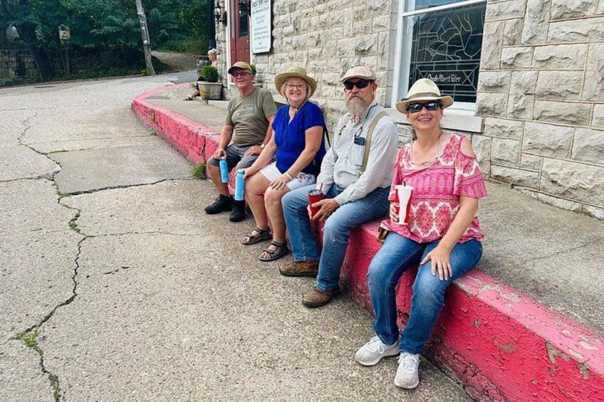 Four people sitting on a red curb in front of a stone building with a window. 2