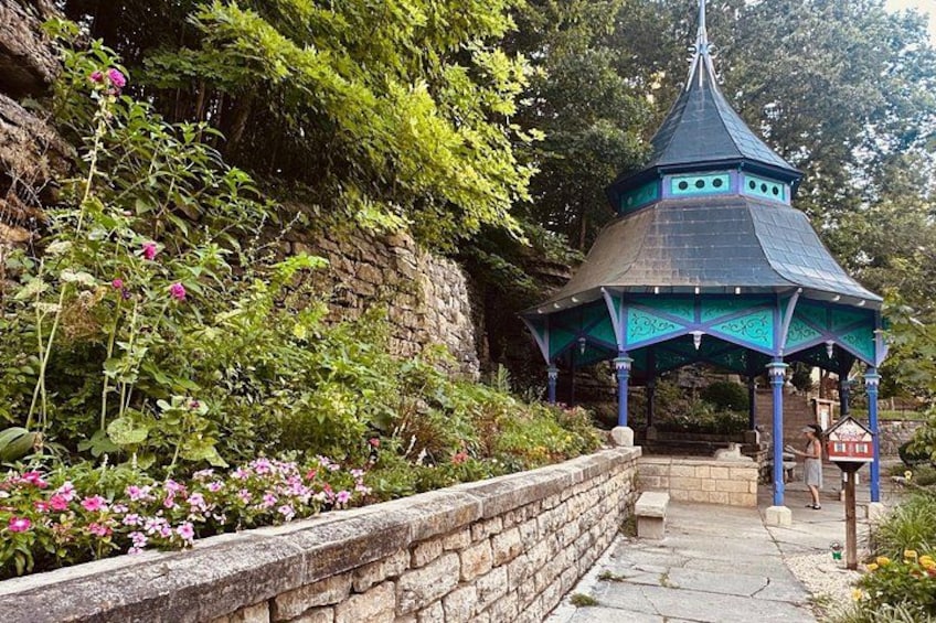 A gazebo with a pointed roof, surrounded by a stone wall and lush greenery. 3