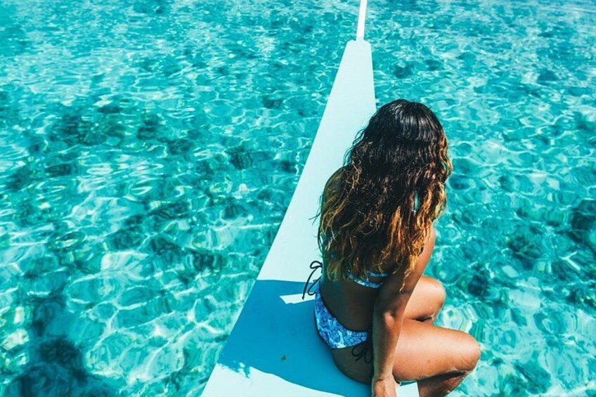 A person sitting on a white board in clear blue water. 1