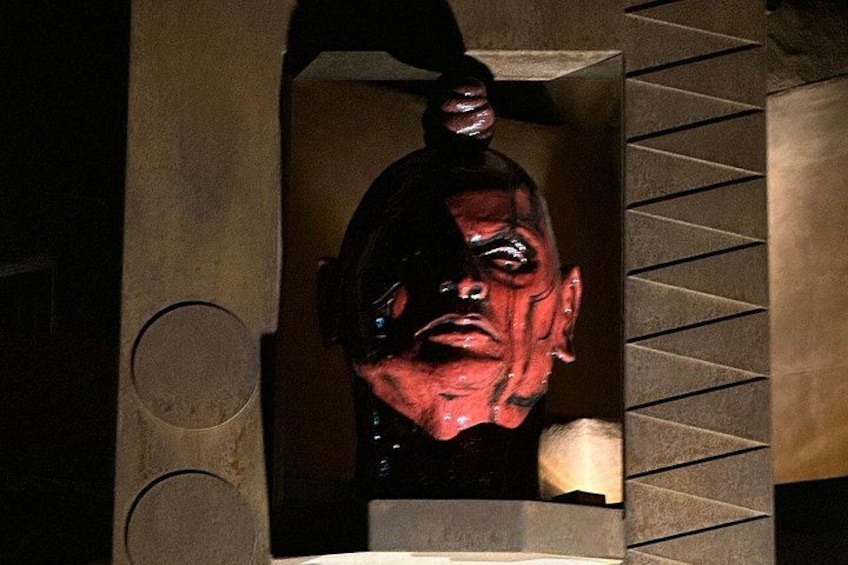 Une sculpture représentant un visage portant un casque, placée dans une niche ornée d’un motif géométrique sur le mur. 3