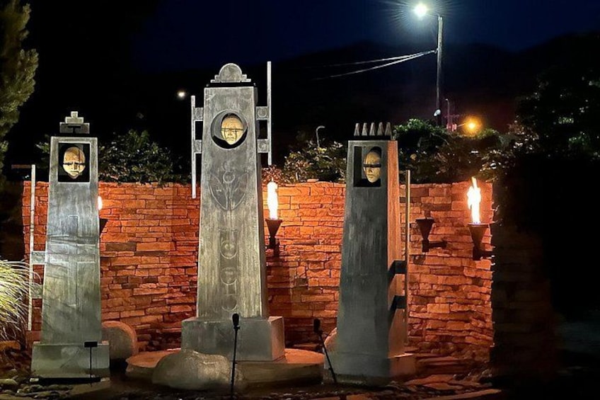 Three illuminated stone structures with circular windows, set against a brick wall at night. 3