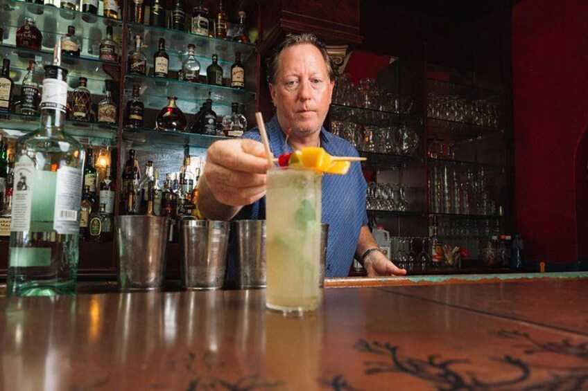 Une personne assise au bar, avec un verre devant elle, entourée d’étagères remplies de bouteilles. 2