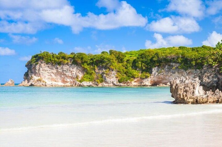 Ein Strand mit klarem türkisblauem Wasser, weißem Sand und einer felsigen Klippe mit grüner Vegetation. 4