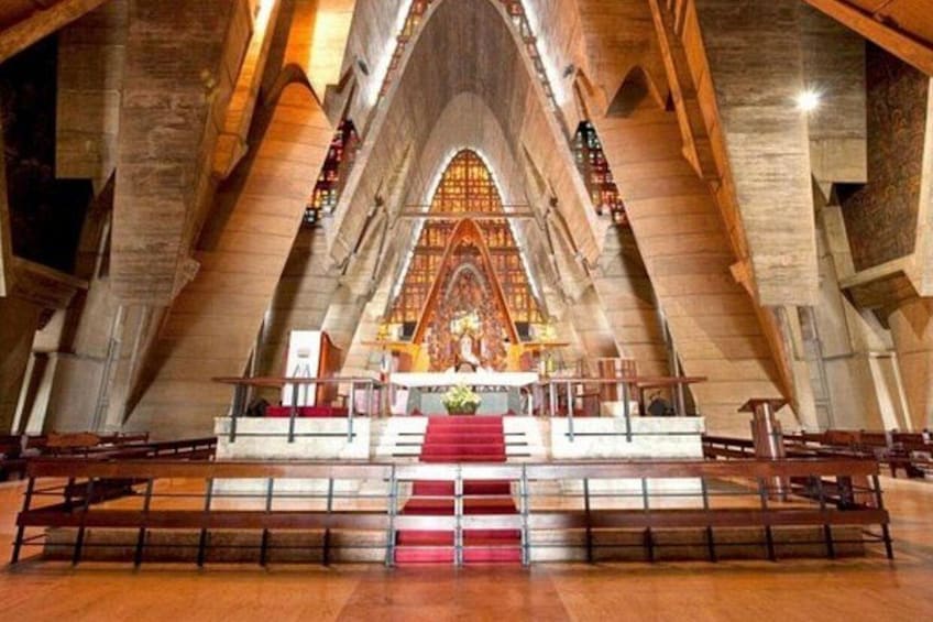 A church interior with a high vaulted ceiling, wooden pews, and a central altar. 3