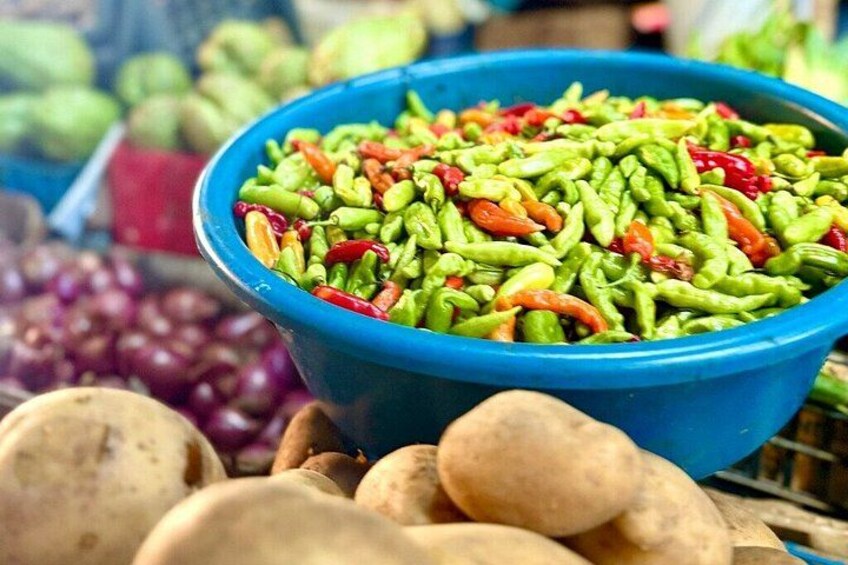 A blue bowl filled with green and red chili peppers, surrounded by potatoes and grapes. 4