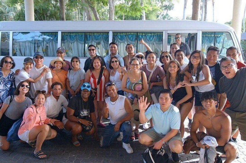 Un grupo de personas posando frente a un autobús blanco con una cortina azul. 3