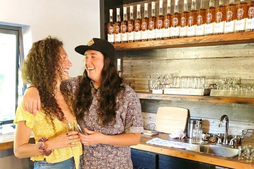 Two people standing at a bar with shelves of bottles and glasses behind them. 3