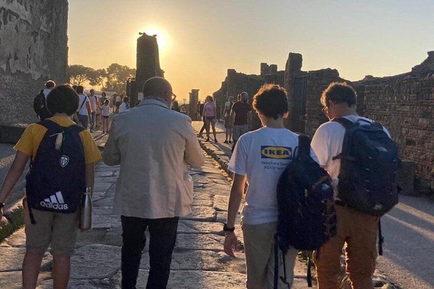 En gruppe mennesker går langs et historisk sted med gamle ruiner og en solnedgang i baggrunden. 5