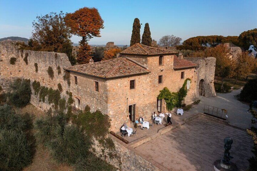 Un edificio histórico de piedra con techo de tejas, rodeado de árboles y un muro de piedra. 2