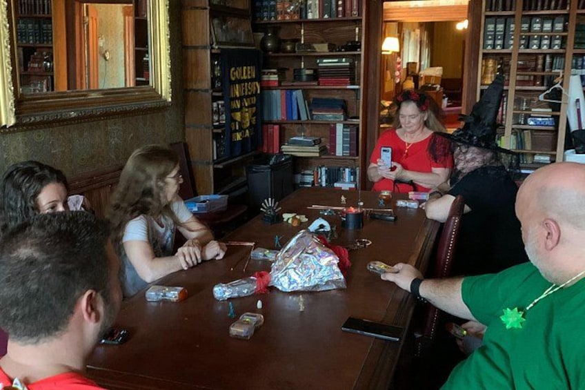 A group of people sitting around a wooden table in a room with bookshelves and a mirror. 2