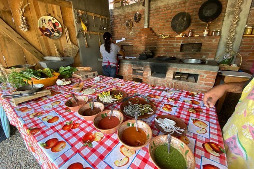 A rustic outdoor kitchen with a brick oven, a table covered with a red and white checkered tablecloth, and various cooking utensils and ingredients. 5
