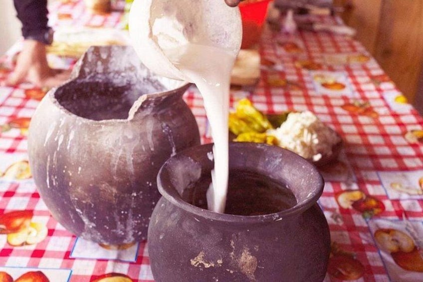 A person pouring a white liquid from a jug into a pot on a checkered tablecloth. 4