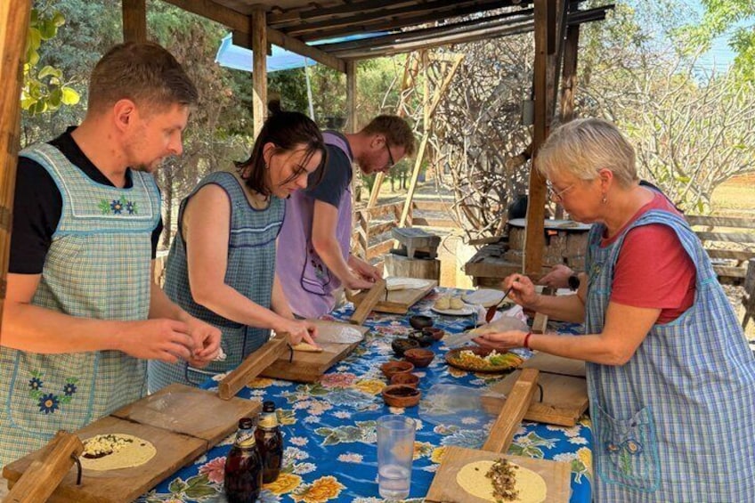 People preparing food outdoors with wooden tables and a blue floral tablecloth. 5