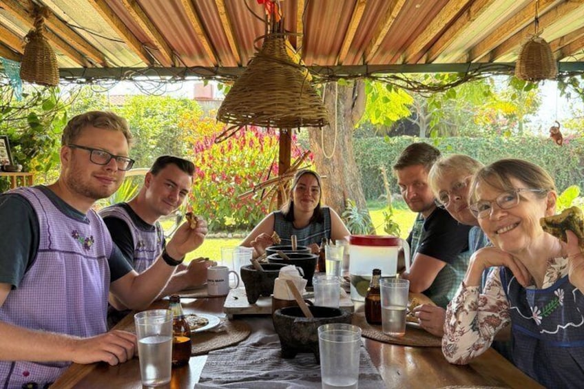 A group of people dining at an outdoor table with a rustic setting, surrounded by greenery. 4