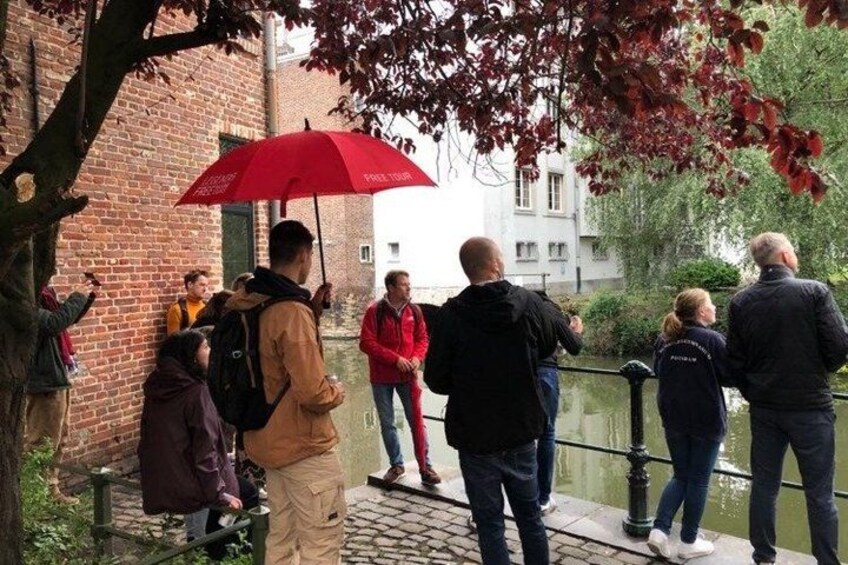 People standing by a canal, some with umbrellas, and a brick building in the background. 3