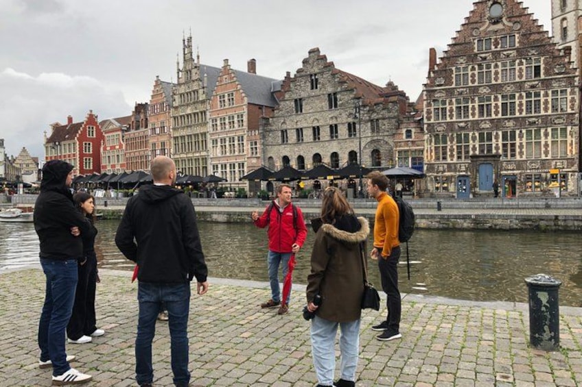 People standing on a cobblestone path by a canal with historic buildings in the background. 2