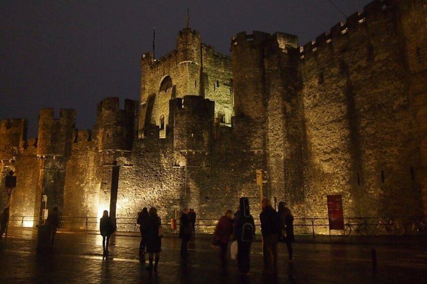 Un castillo de piedra histórico iluminado de noche, con torres brillantes y un foso. 4