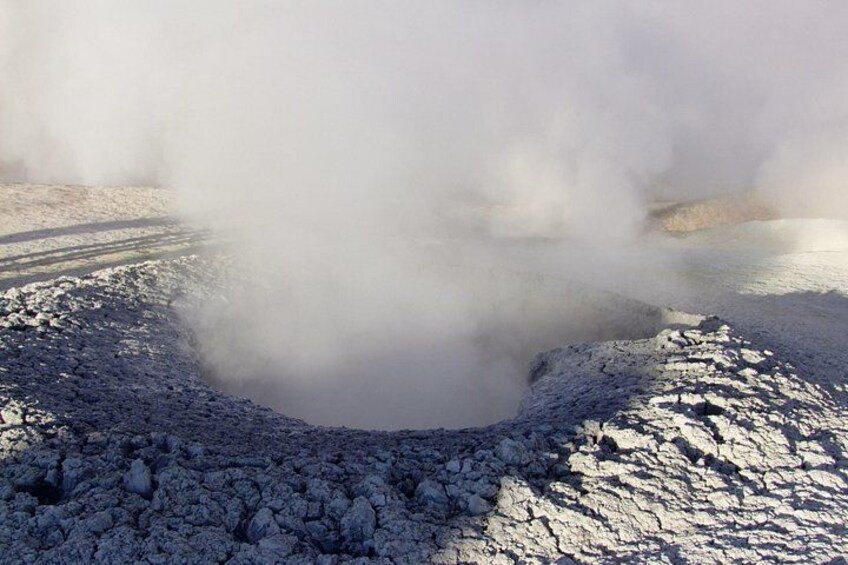 A geothermal area with steam rising from a crater surrounded by rocky terrain. 3