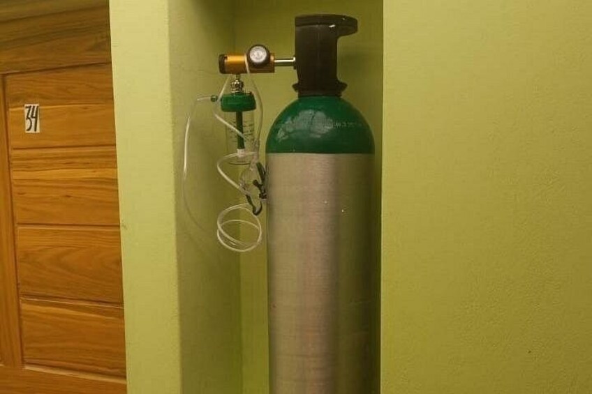 A green oxygen cylinder with a valve and tubing against a green wall. 2