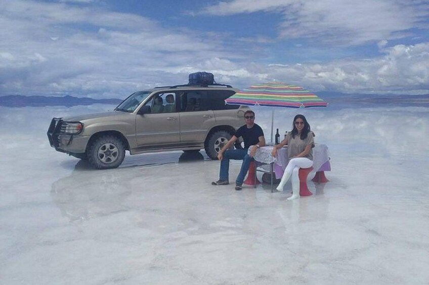 A beige SUV parked on a flat, white surface with a colorful striped umbrella and a table nearby. 5