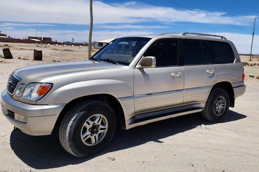 A silver SUV parked on a sandy surface with a clear sky in the background. 2
