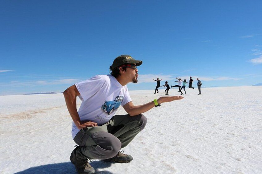 A person crouching on a salt flat with a clear sky, and several people in the background. 4