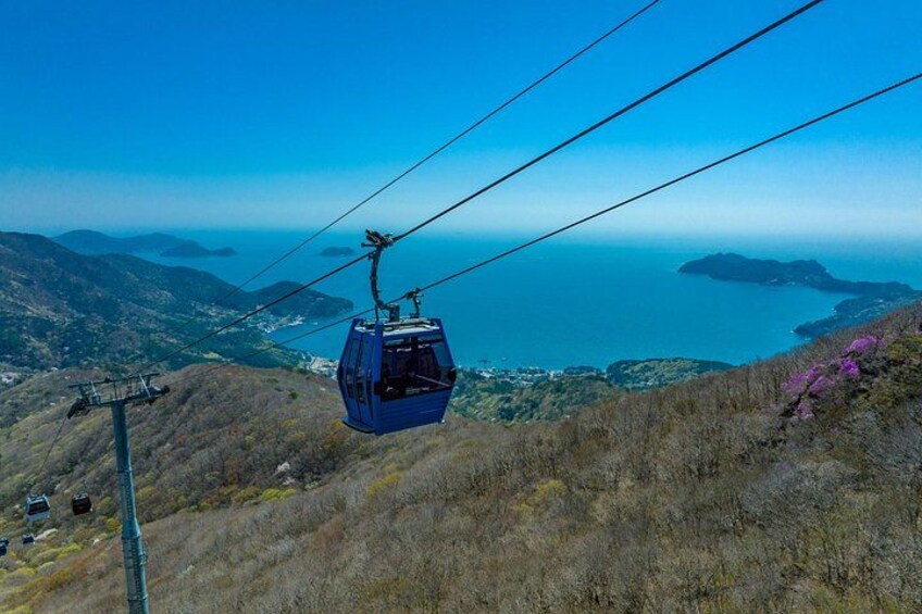 A cable car ascending a mountain with a view of the ocean and hills in the background. 2