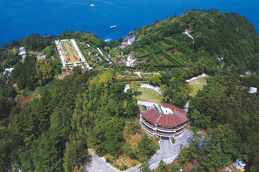 A circular building surrounded by dense forest, a landscaped area with geometric patterns, and a coastline with boats. 3