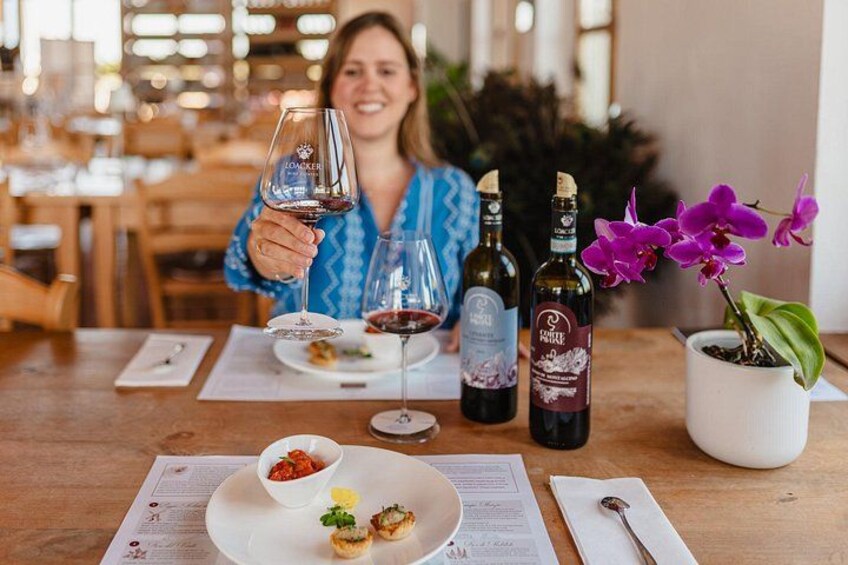 A dining table with wine bottles, a glass of red wine, a plate with food, and a potted orchid. 3