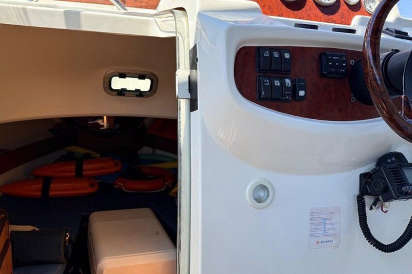 A boat's interior with a steering wheel, control panel, life jackets, and a cushion. 2