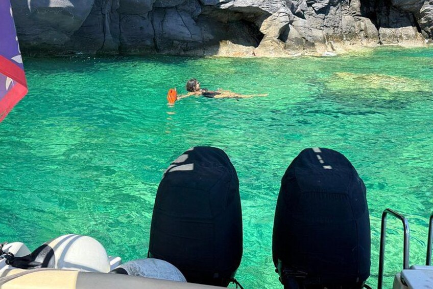 A person swimming in clear turquoise water, with rocky cliffs in the background. 5