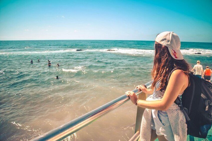 Een strand met mensen die zwemmen en een persoon op een reling staat. 2